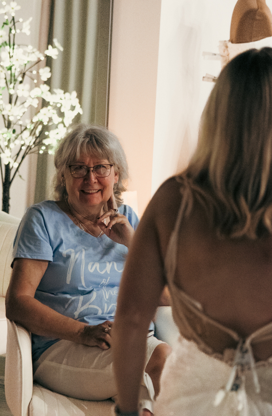 image shows a woman smiling watching her family member trying on wedding dresses