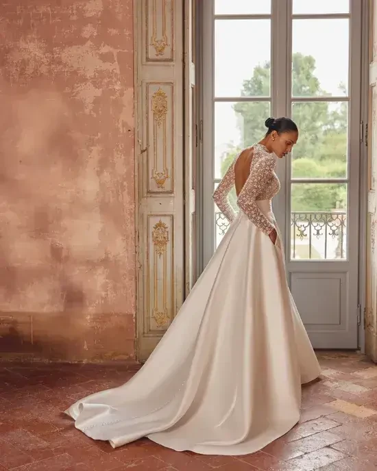 Model is wearing a mikado A-line gown with a high collar neckline and a beaded bodice, combining regal elegance with subtle sparkle.