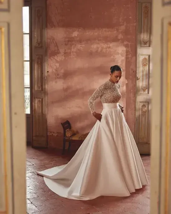 Model is wearing a mikado A-line gown with a high collar neckline and a beaded bodice, combining regal elegance with subtle sparkle.