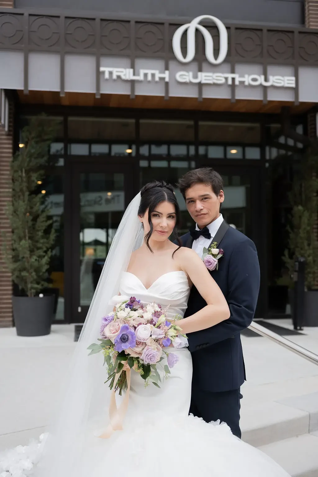 model is wearing a strapless mermaid wedding dress and another model wearing a black tux