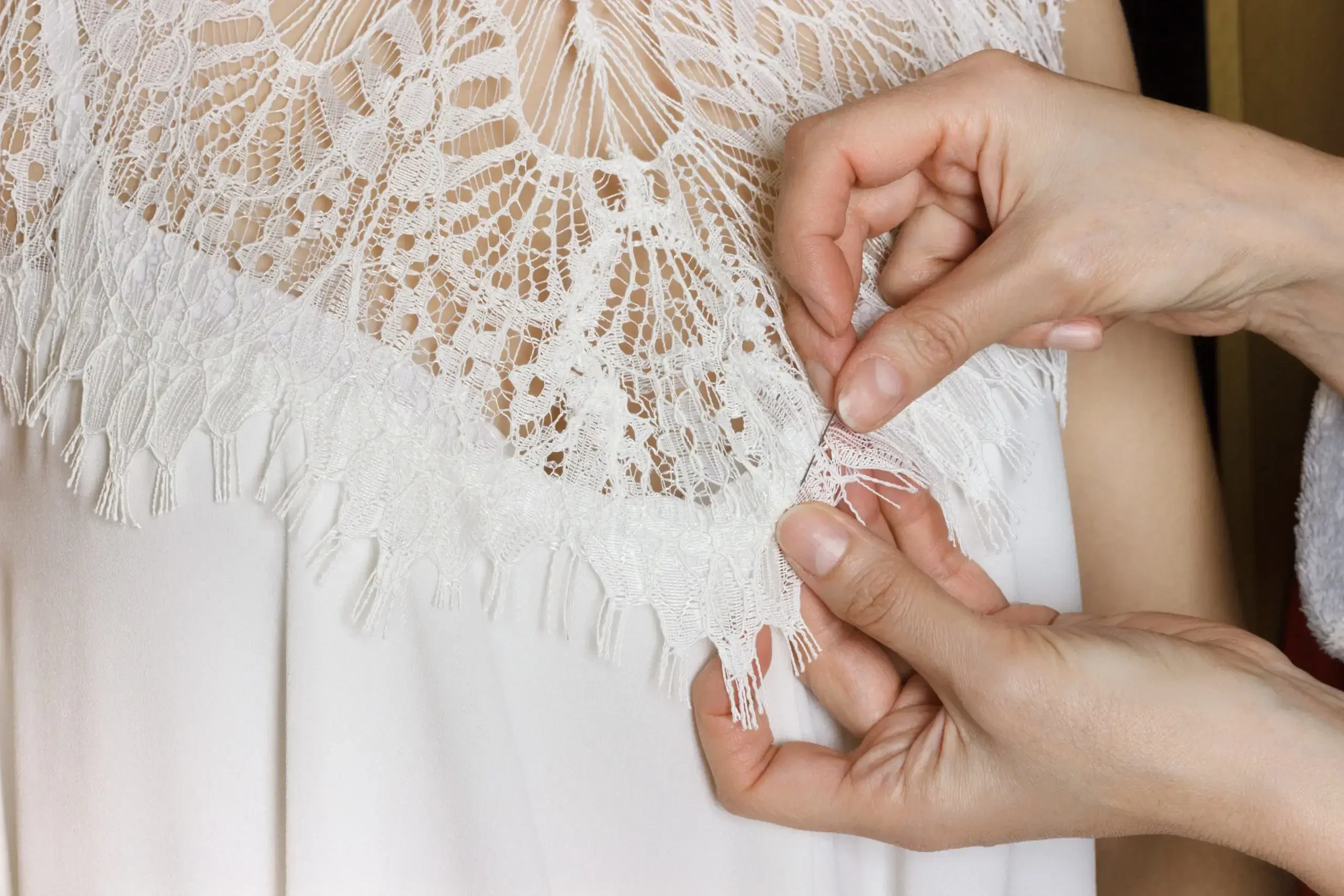 A close-up of a person adjusting a delicate lace trim on a garment.