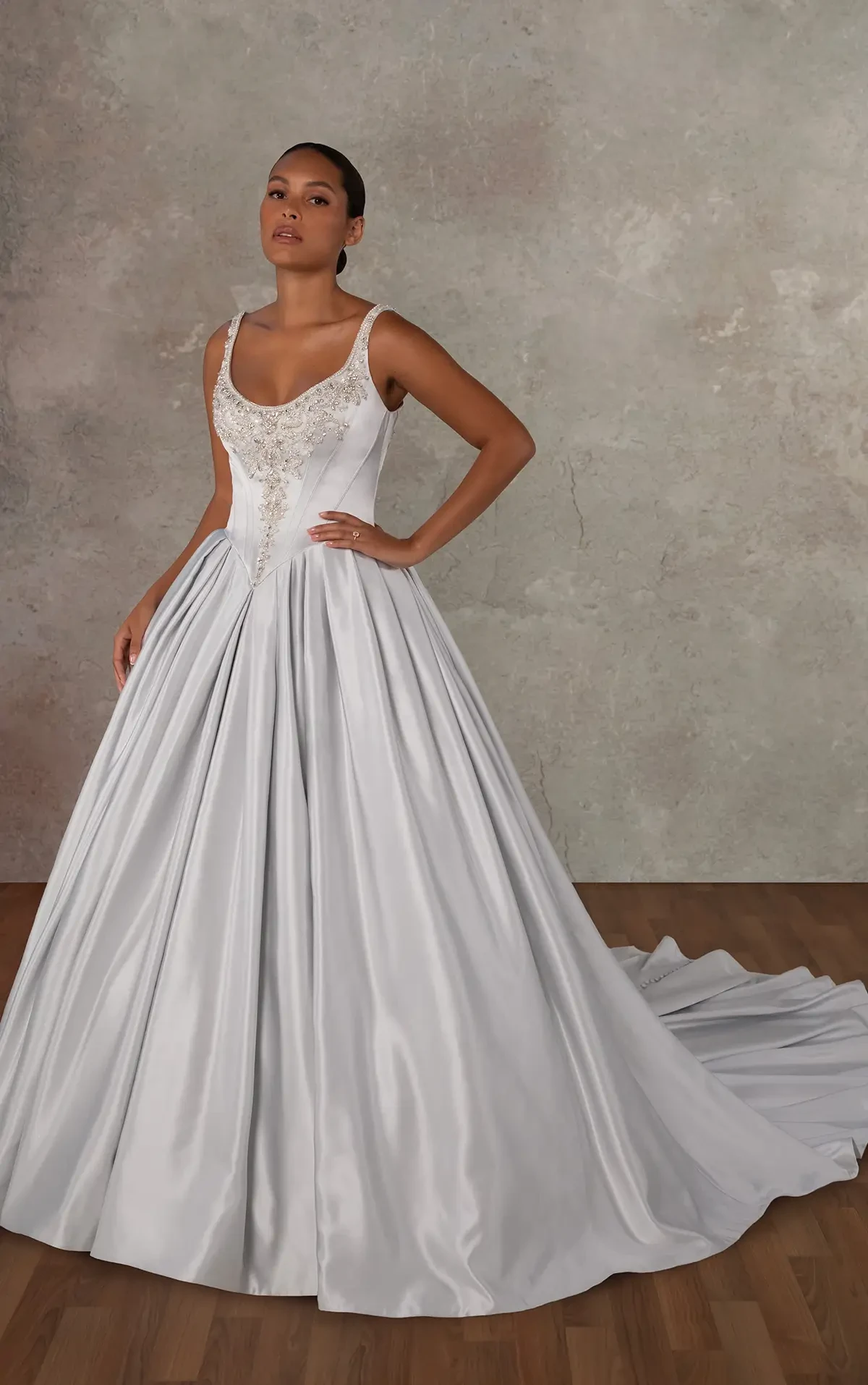 A woman in an elegant white ball gown with intricate lace detailing on the bodice stands confidently against a neutral backdrop, conveying grace and sophistication.