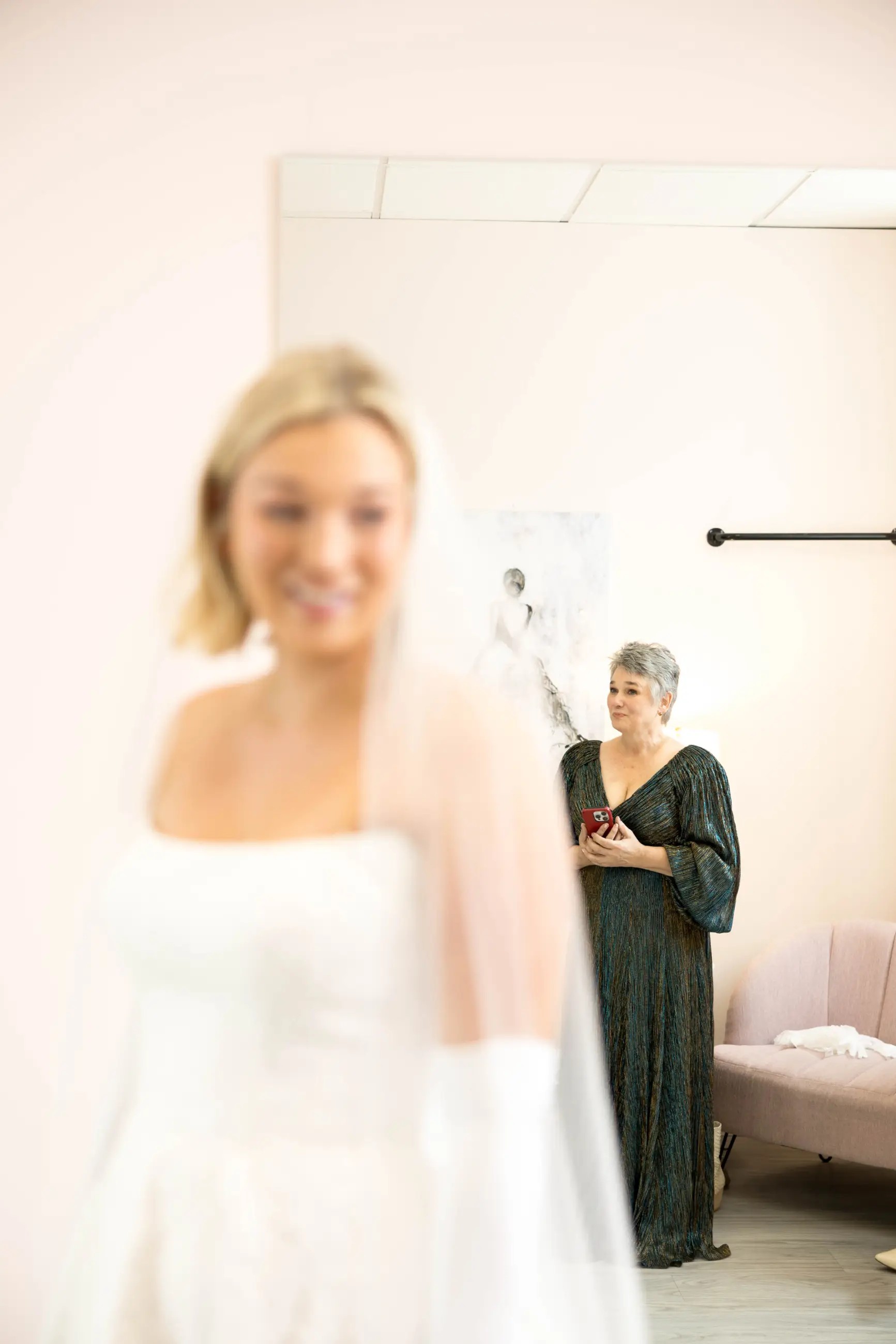 image shows a bride with her mom in the background looking lovingly at her