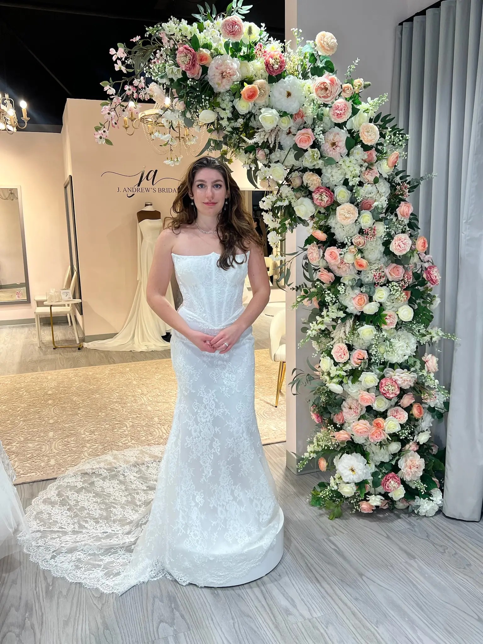 Model is wearing a fit and flare wedding dress with a strapless corset bodice and allover lace on the skirt
