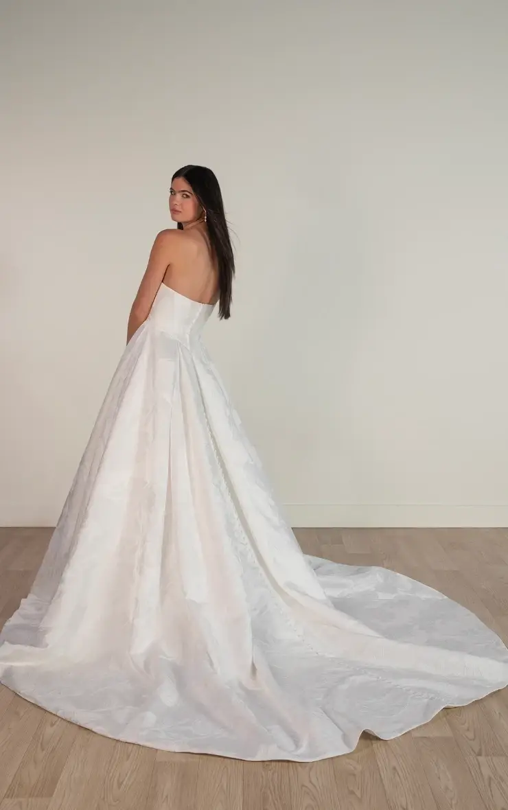 Model is wearing a strapless satin ballgown with a ruched neckline, Basque waist, and a pleated skirt made for fairytale winter celebrations.